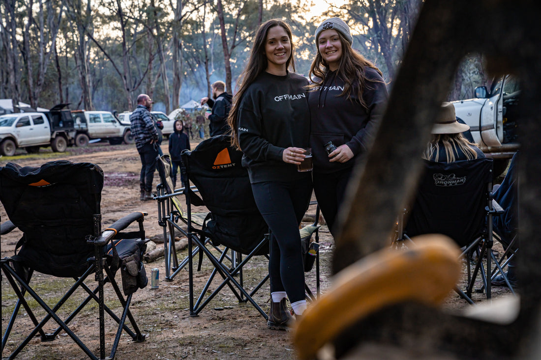 Offmain girls wearing their black hoodie, enjoying their drinks in a campsite.