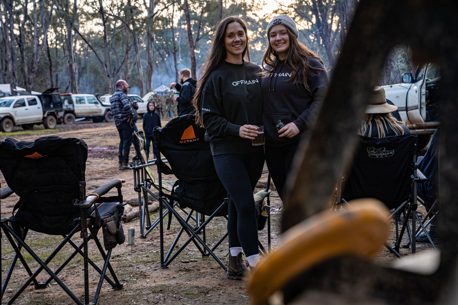 Offmain girls wearing their black hoodie, enjoying their drinks in a campsite.